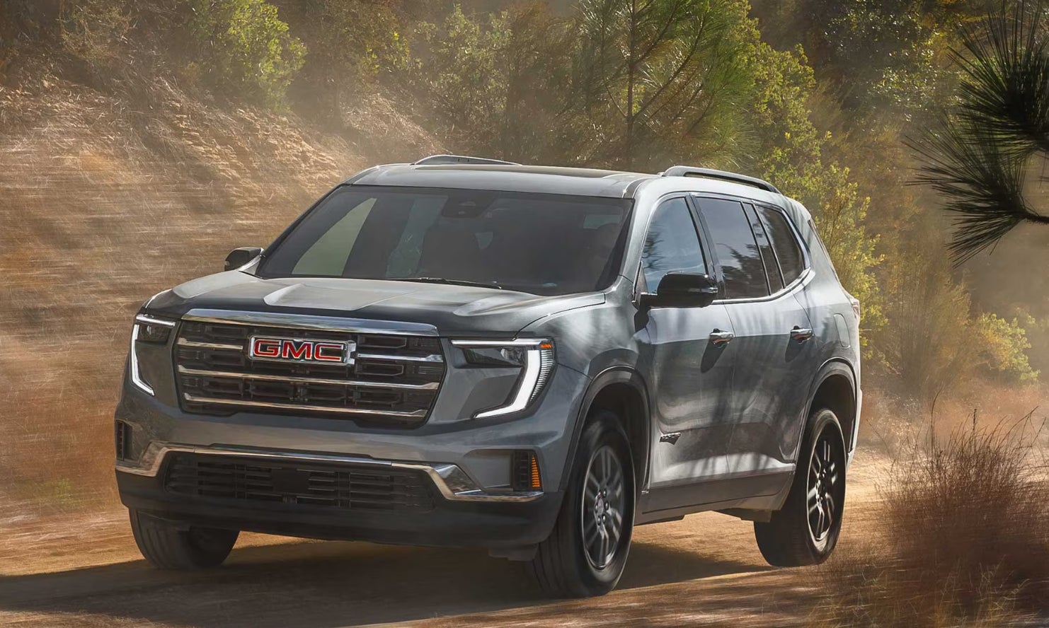 A gray GMC Acadia driving on a dirt road.
