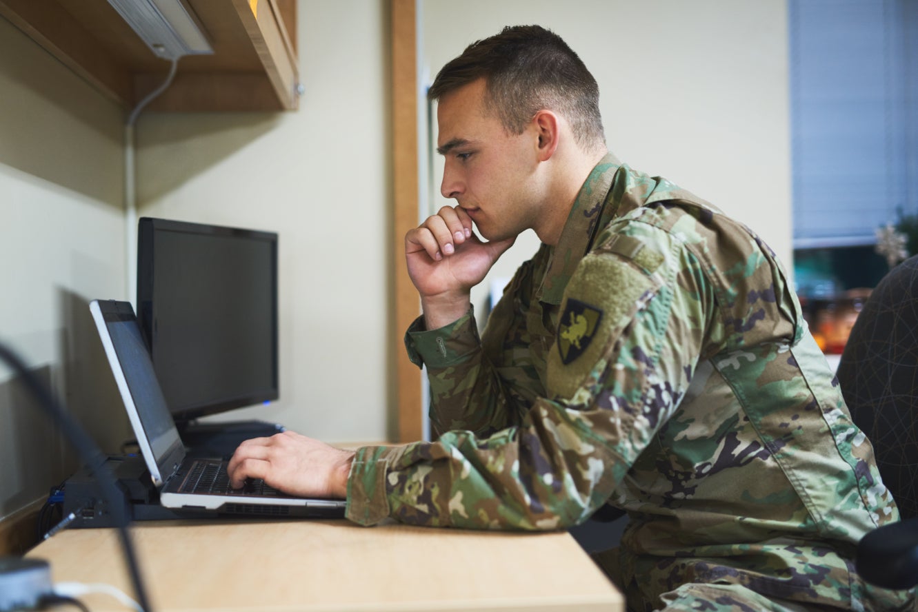 A member of the military sitting at a desk on a laptop.
